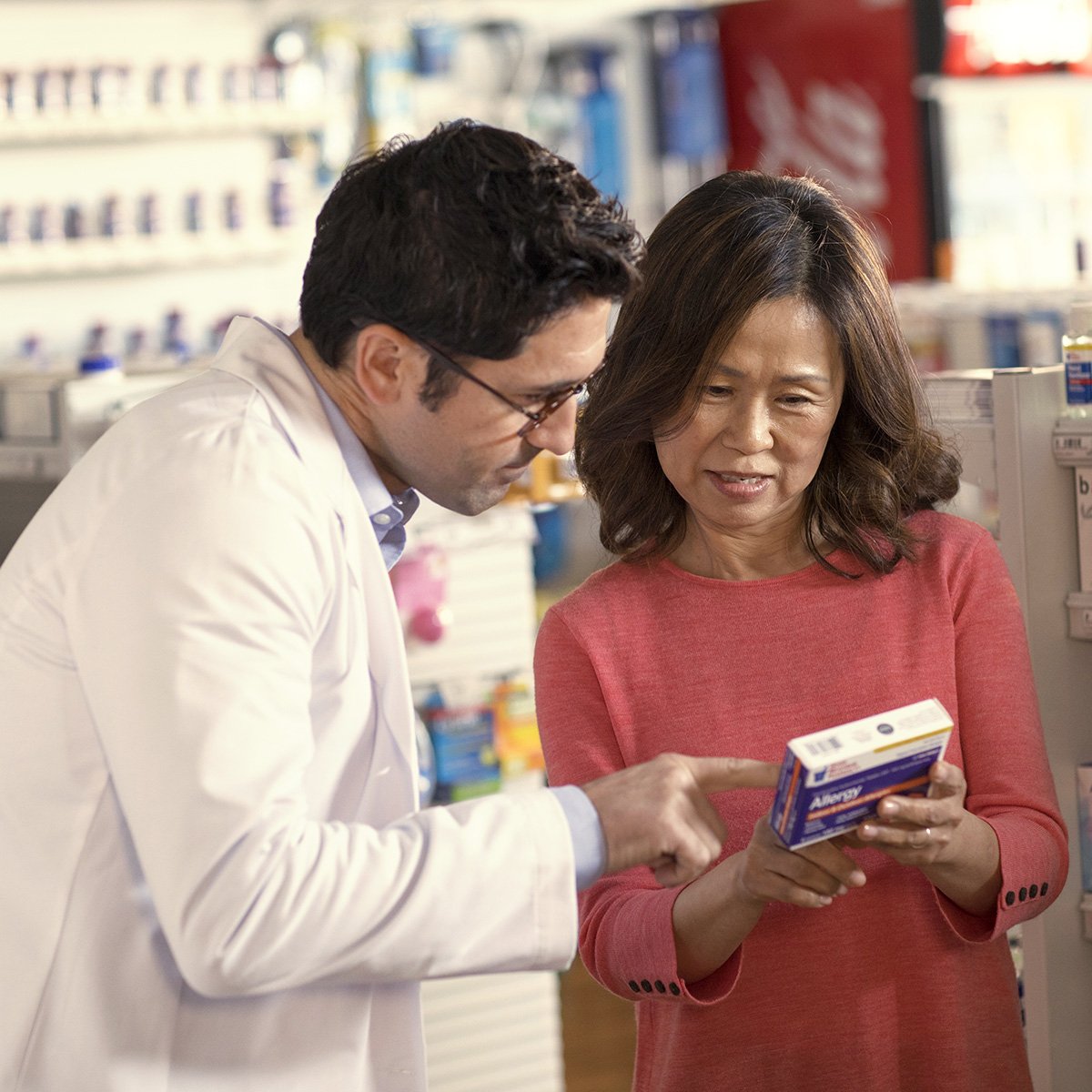 A pharmacist stands next to a patient helping her review and understand a box of medication she’s holding.