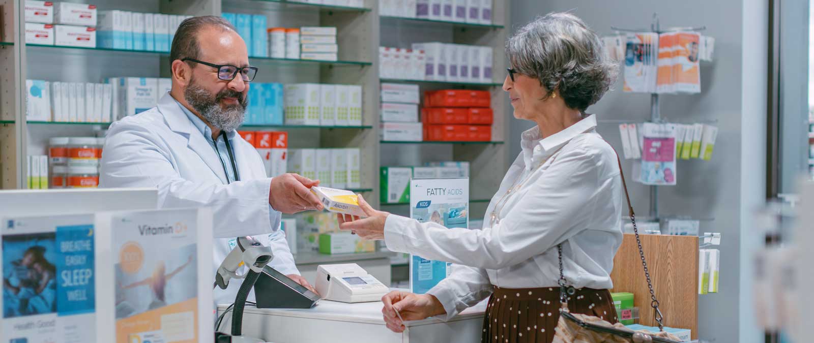 Pharmacist handing a box of medication to a woman at a pharmacy counter.