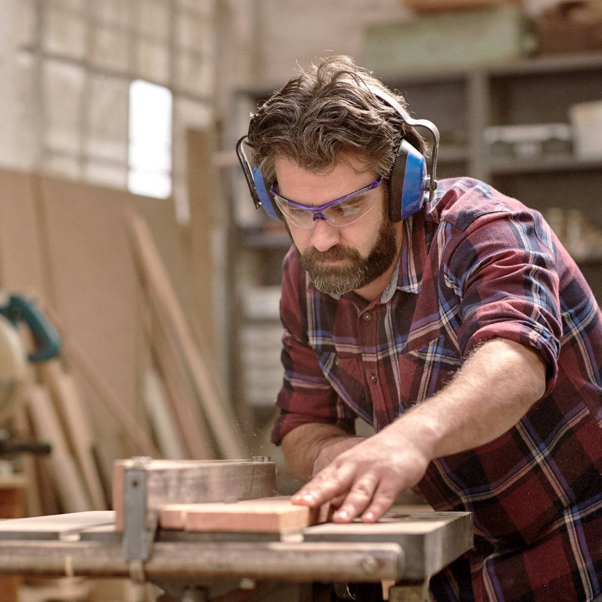 Hombre con barba cortando madera con una sierra de mesa.