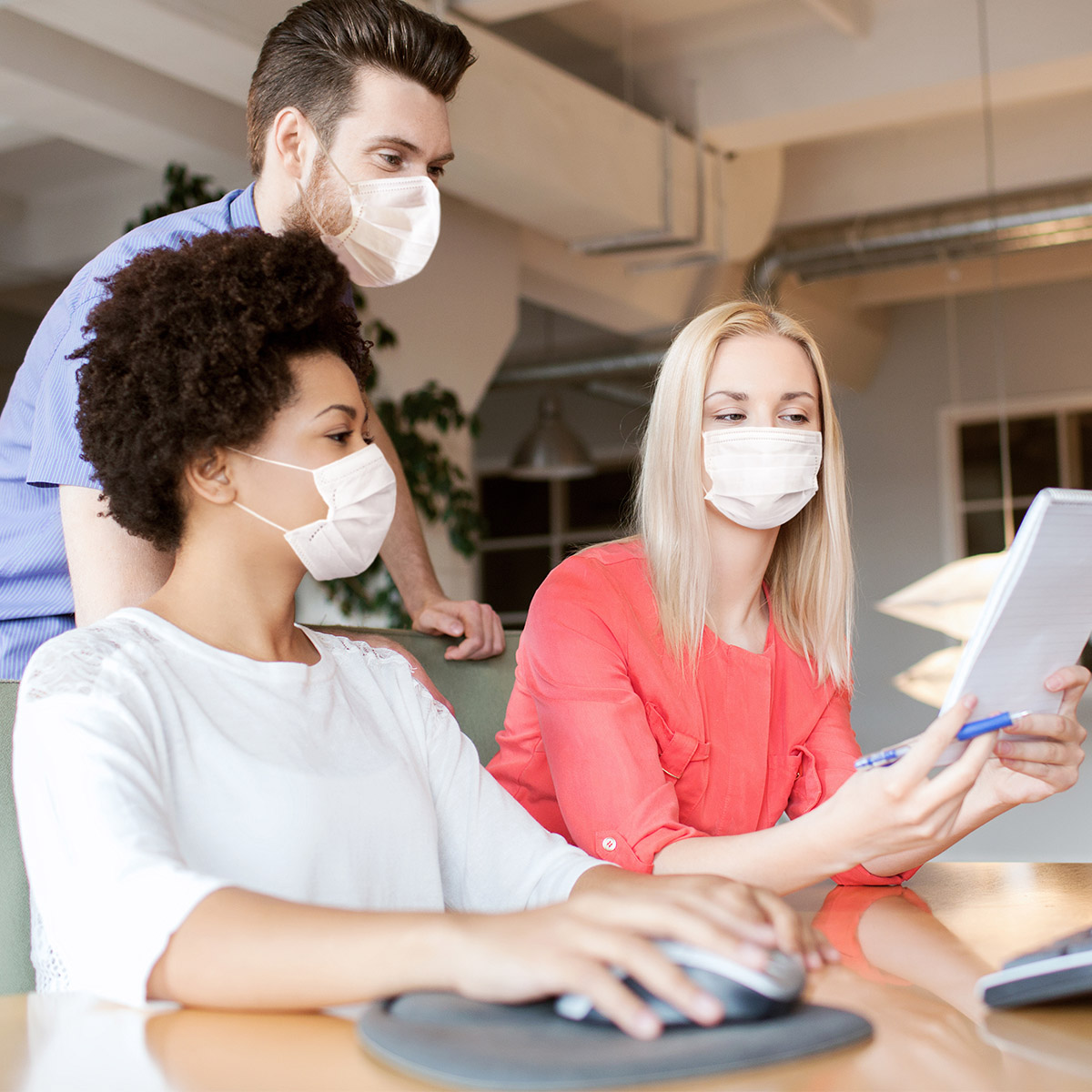 3 people wearing masks look at a tablet while using a computer.