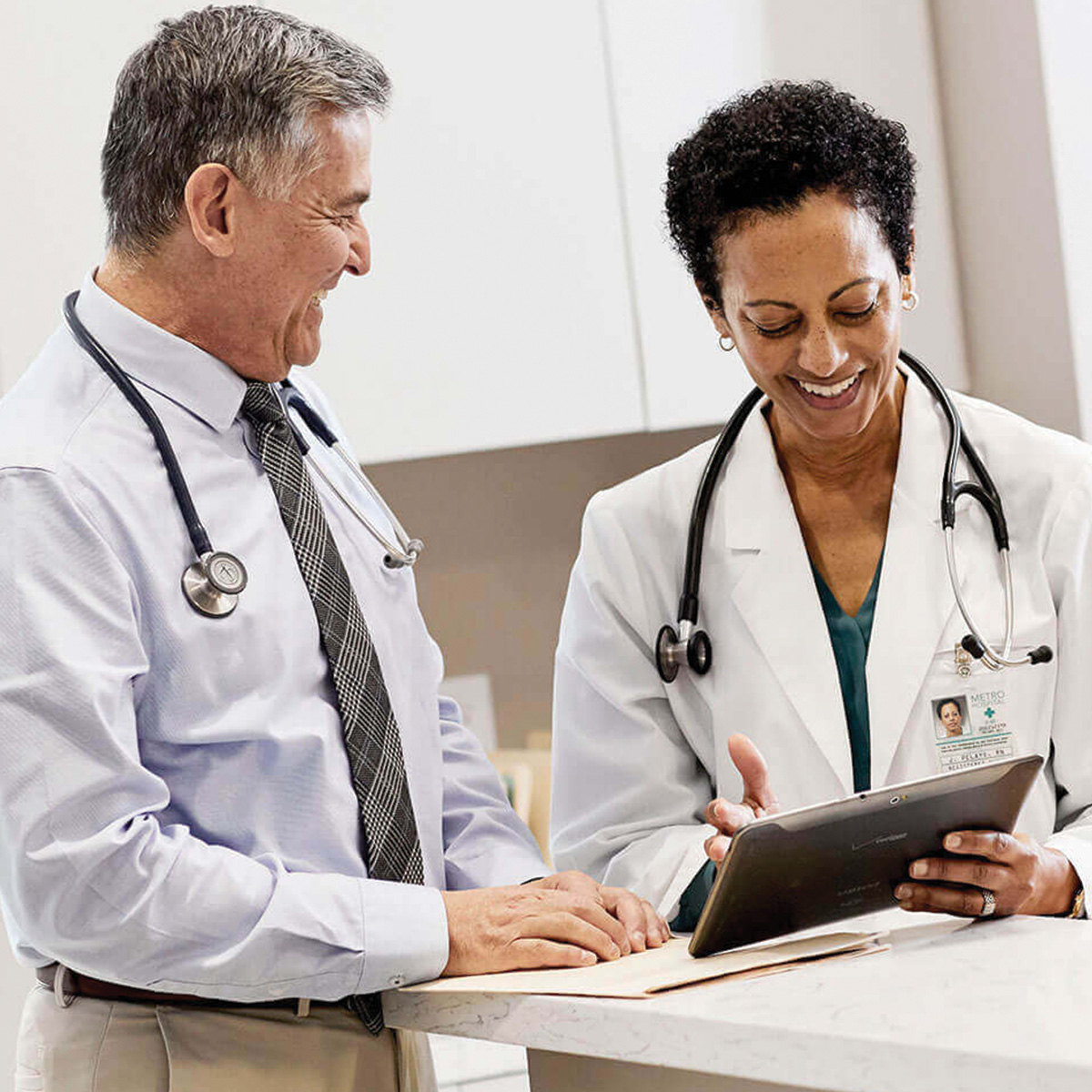 Two doctors smile as they discuss information on a tablet.