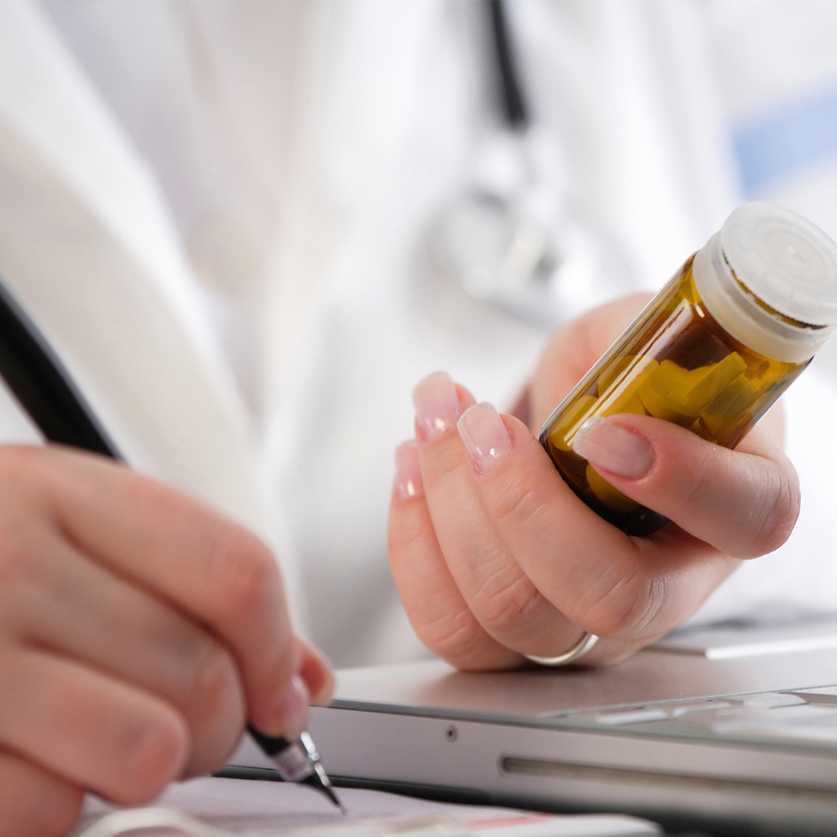 A physician holds a vial of pills while taking notes at a computer.