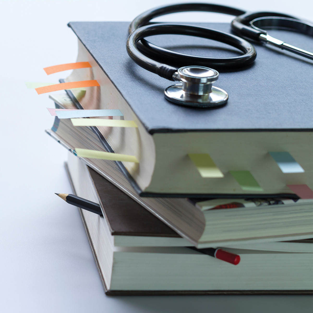Libros de medicina con varias etiquetas de colores y un estetoscopio apoyado arriba.
