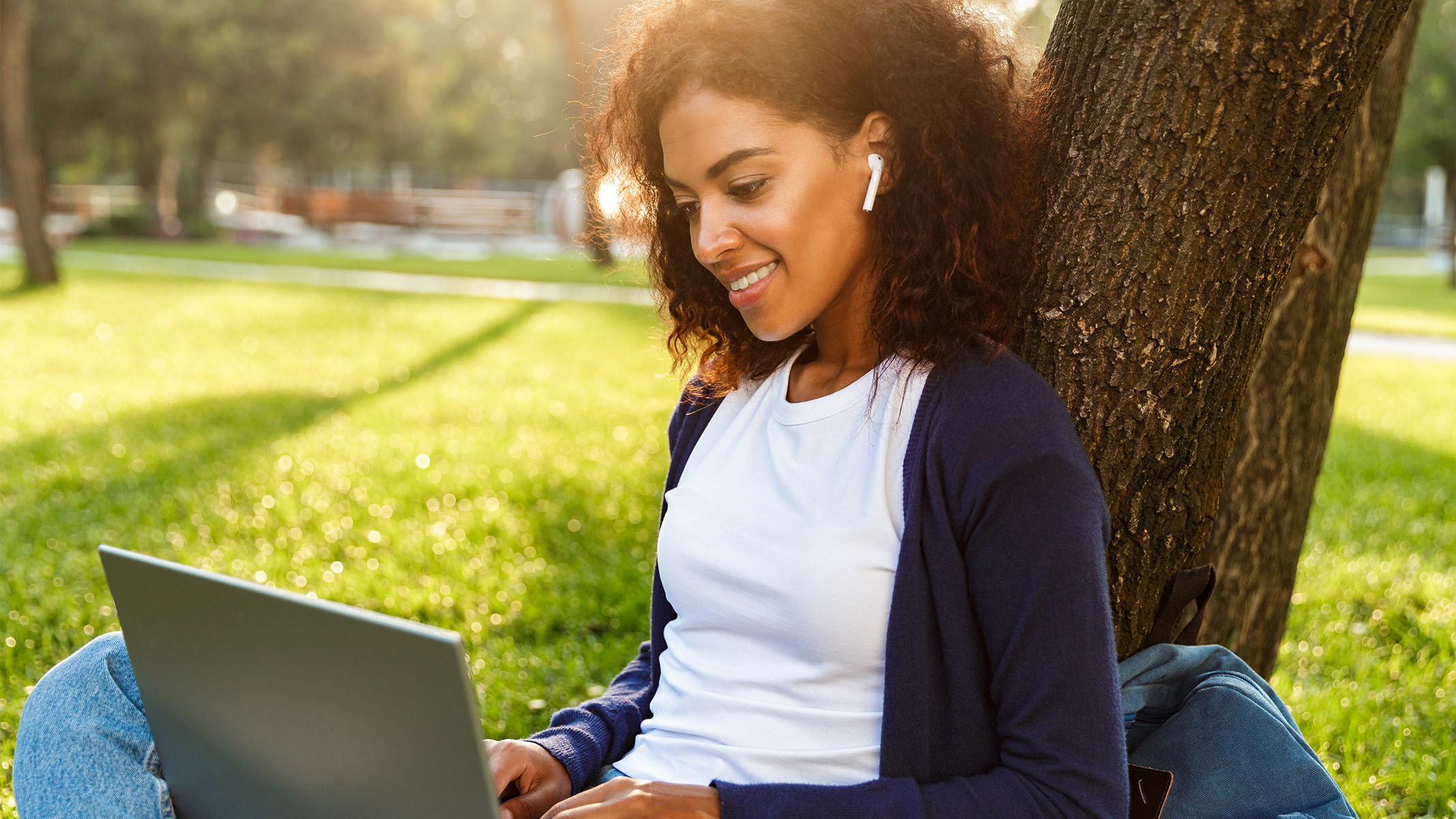 Young woman sitting outside listening to music while working on her laptop