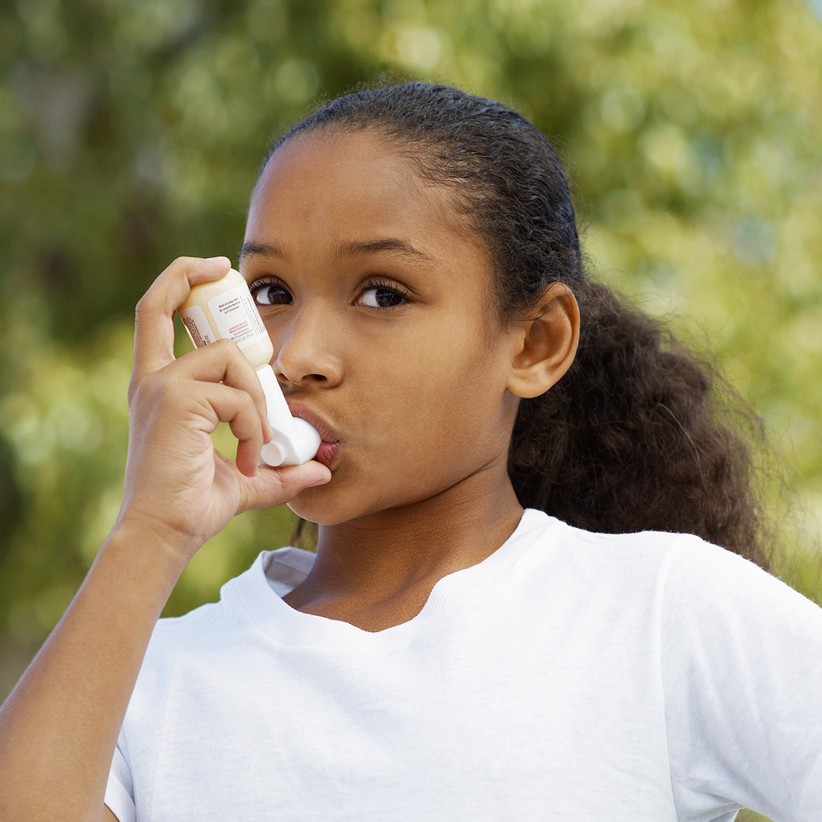 Young girl using her inhaler outside.