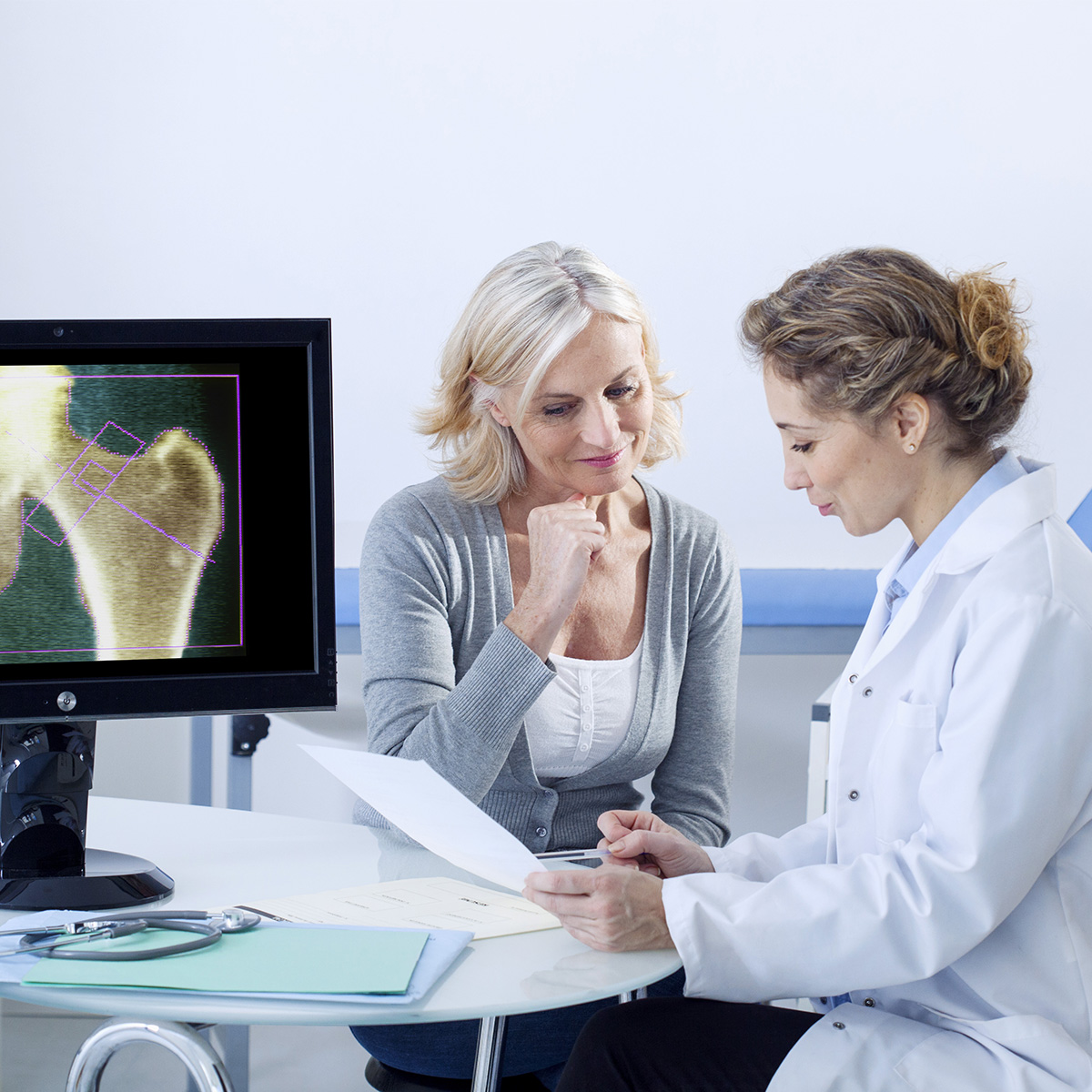Una mujer habla con su médico cerca de una radiografía de un hueso de la cadera.