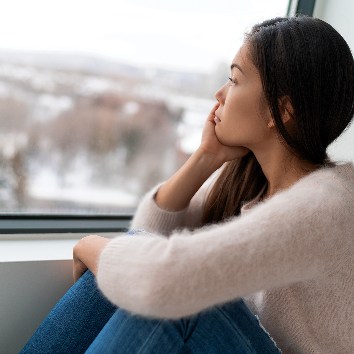 Una mujer contempla con mirada triste el exterior a través de su ventana.