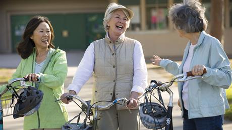 3 women laugh as they stand next to their bicycles.