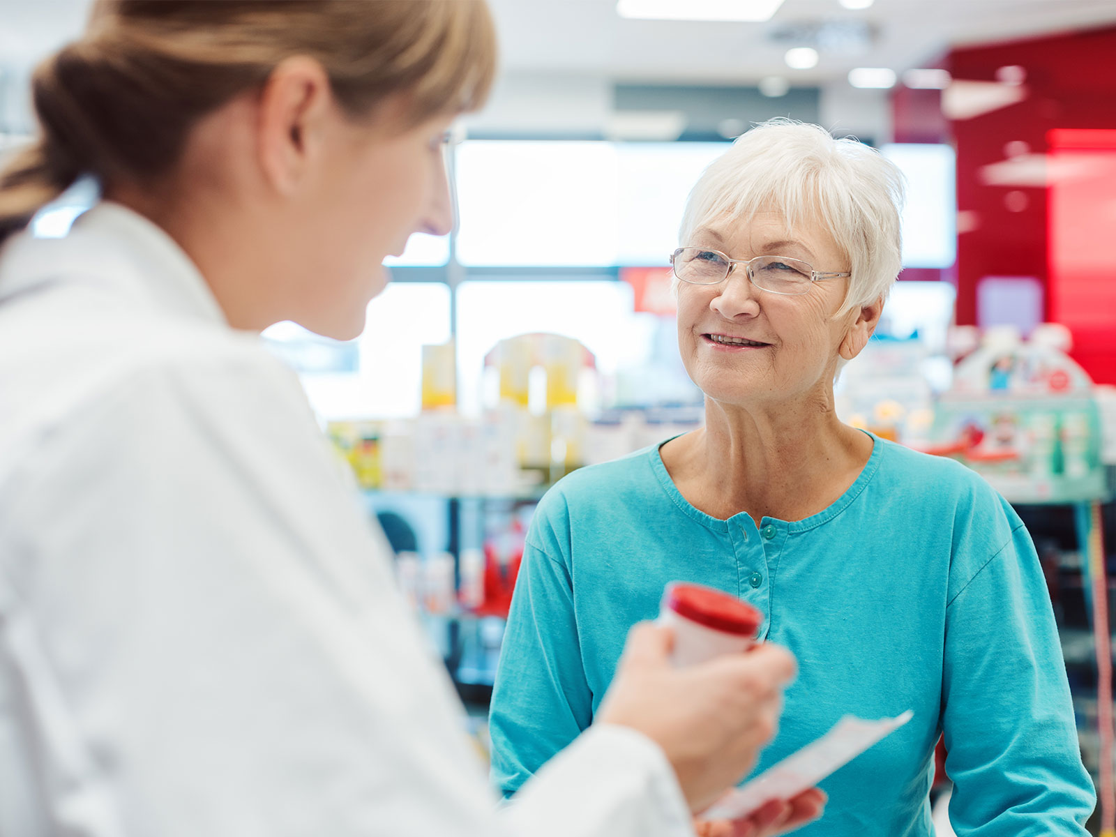 Mujer mayor escuchando consejos sobre medicamentos en una farmacia.