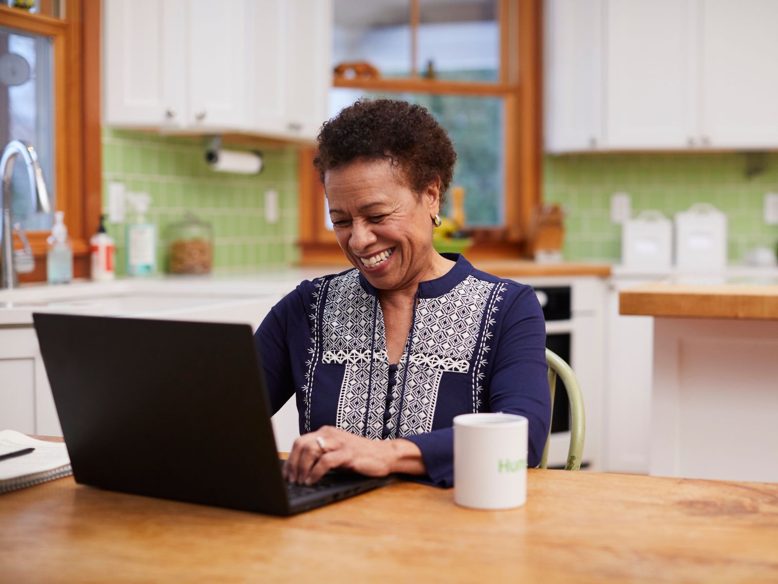 Woman smiling and using a laptop at a table.