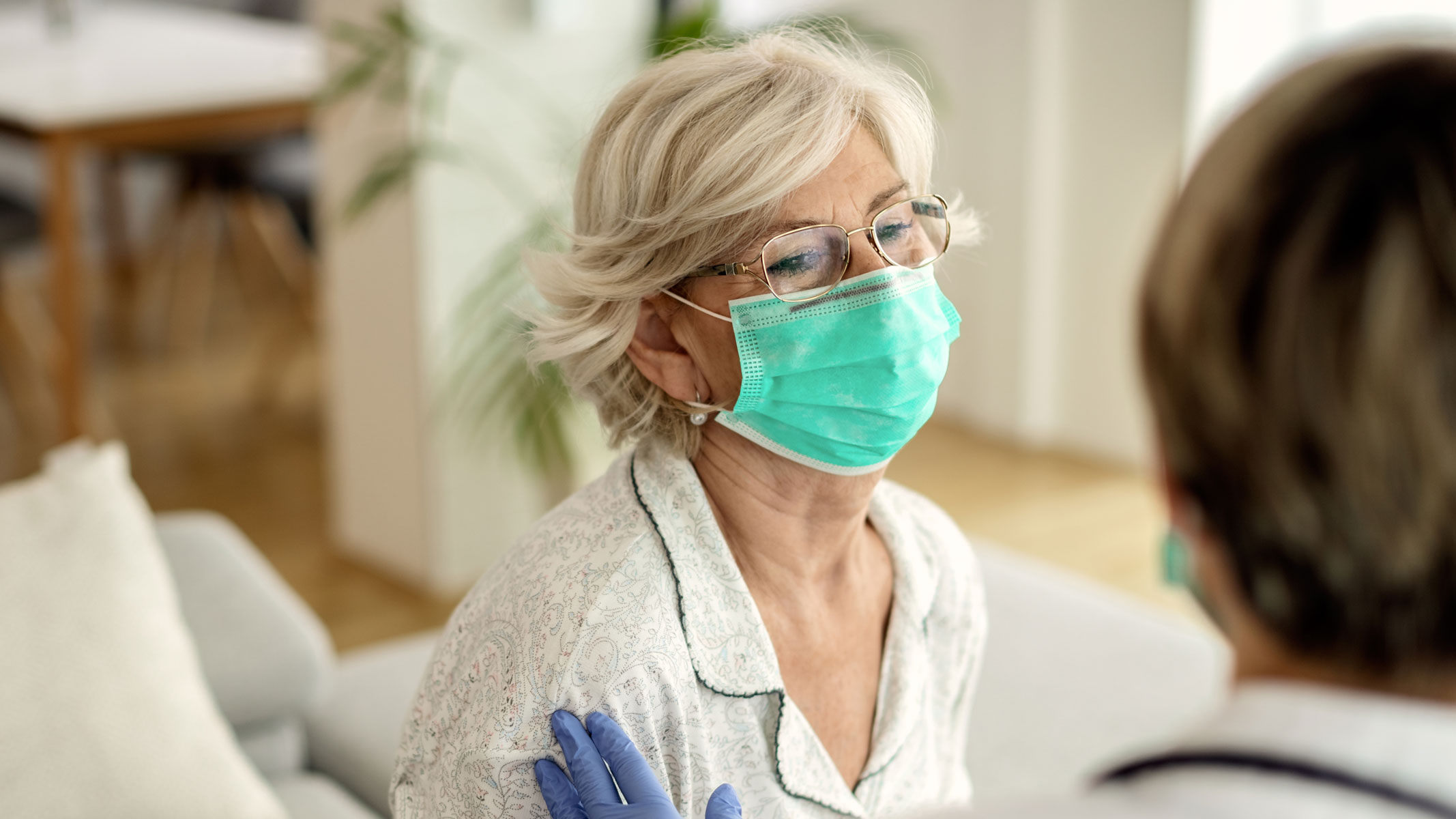 Older woman in mask sitting with medical professional.
