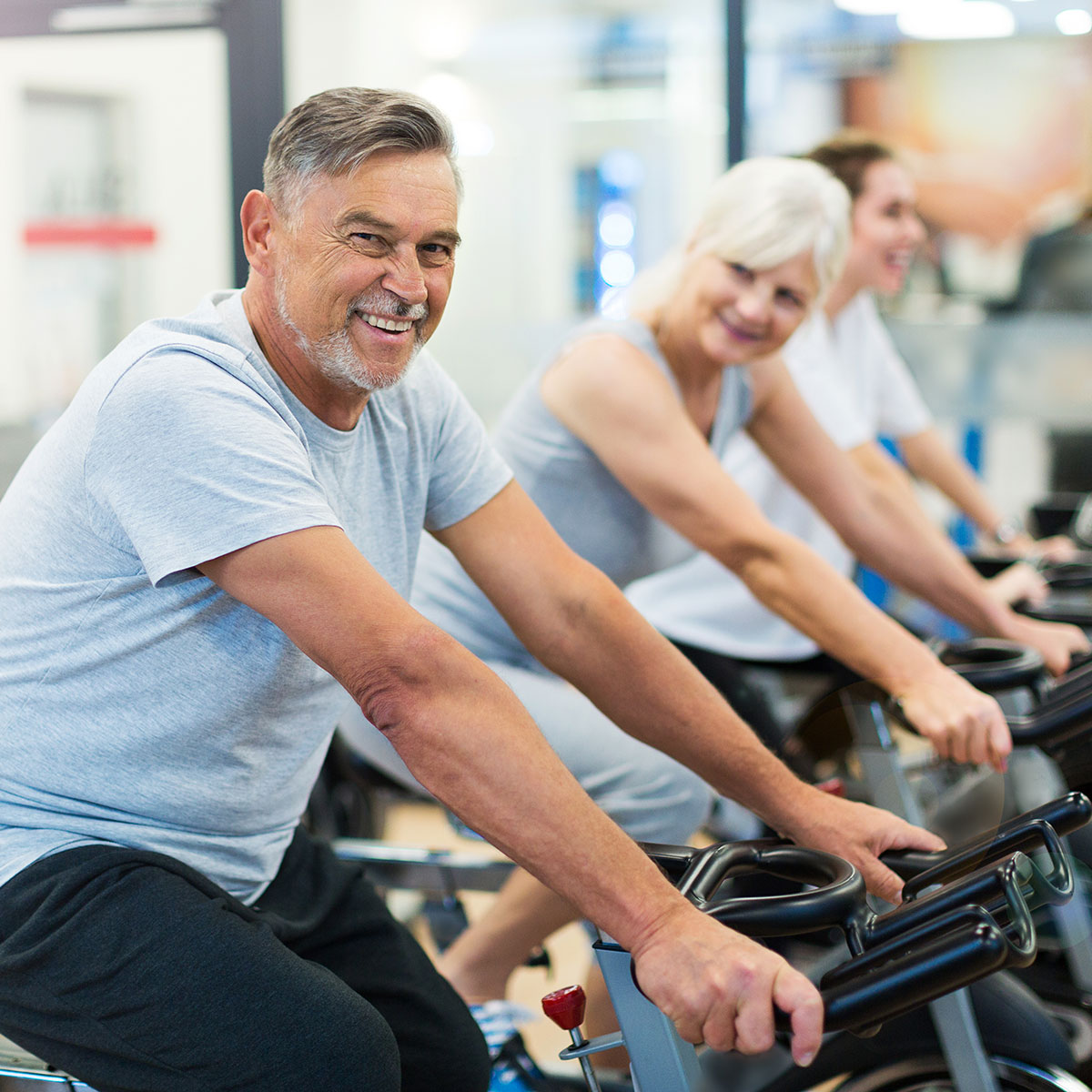 A man and a woman ride exercise bikes at a fitness facility.