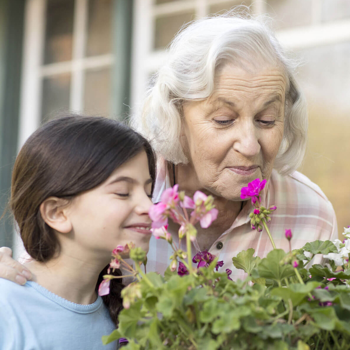Abuela y nieta oliendo flores fuera de la casa.