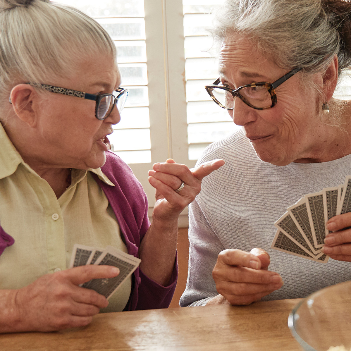Two women sitting at table talking and playing cards