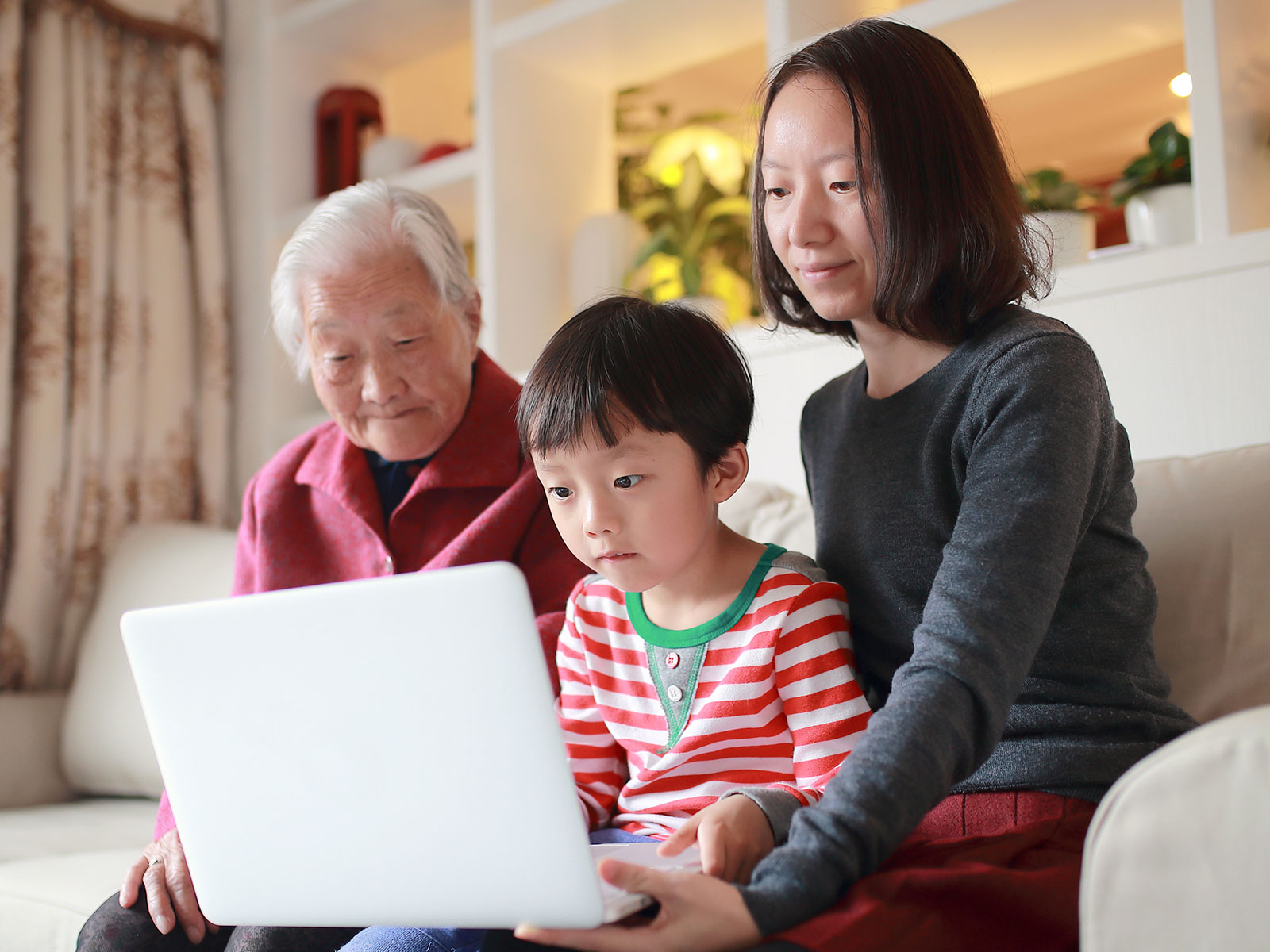 A woman and child work on a laptop while a grandparent looks on.