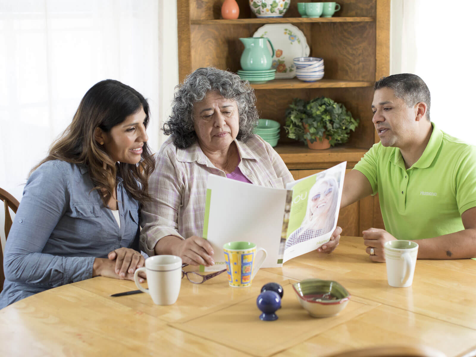 A Humana employee communicates in Spanish to an elderly woman and her daughter as she assists them in understanding a healthcare pamphlet.