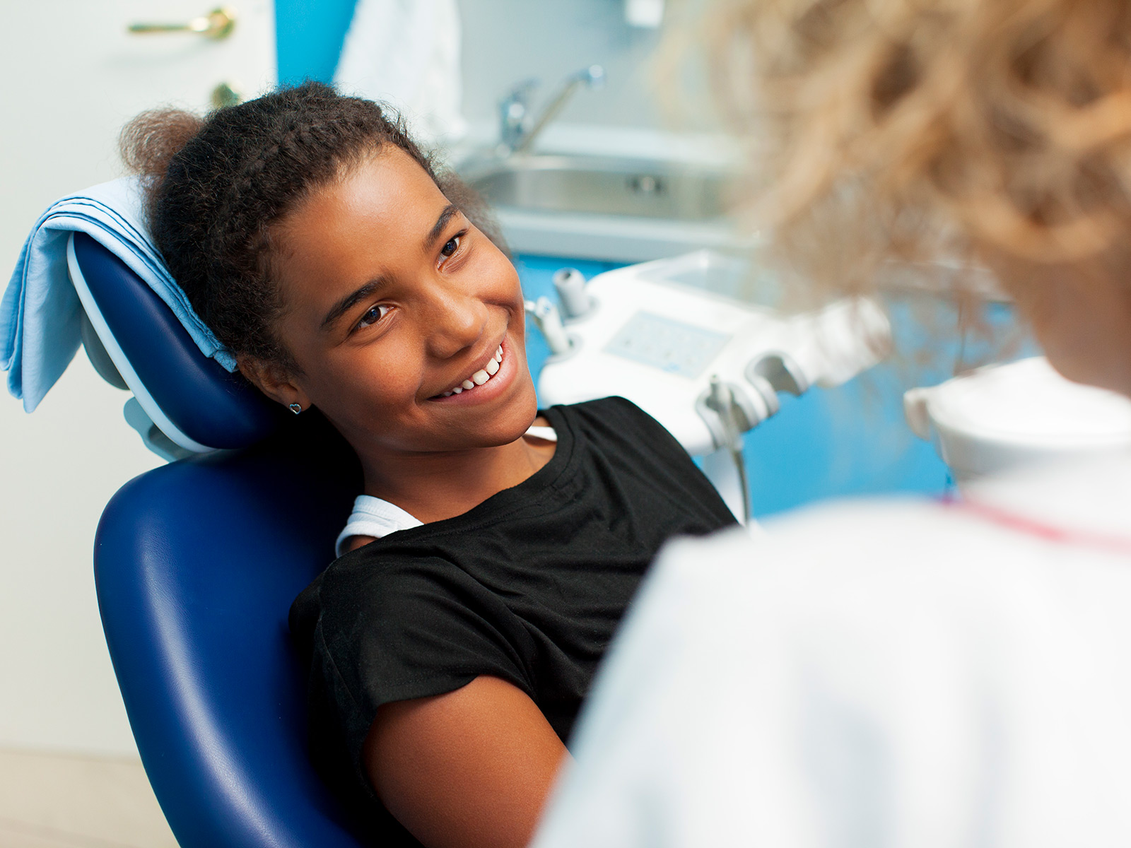 Child smiles as she listens to a dental healthcare provider.