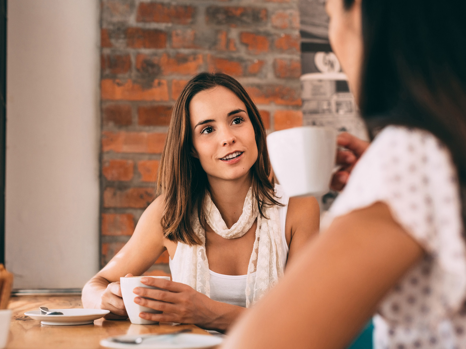 Una mujer joven sostiene una taza de té mientas habla con otra mujer en una cafetería