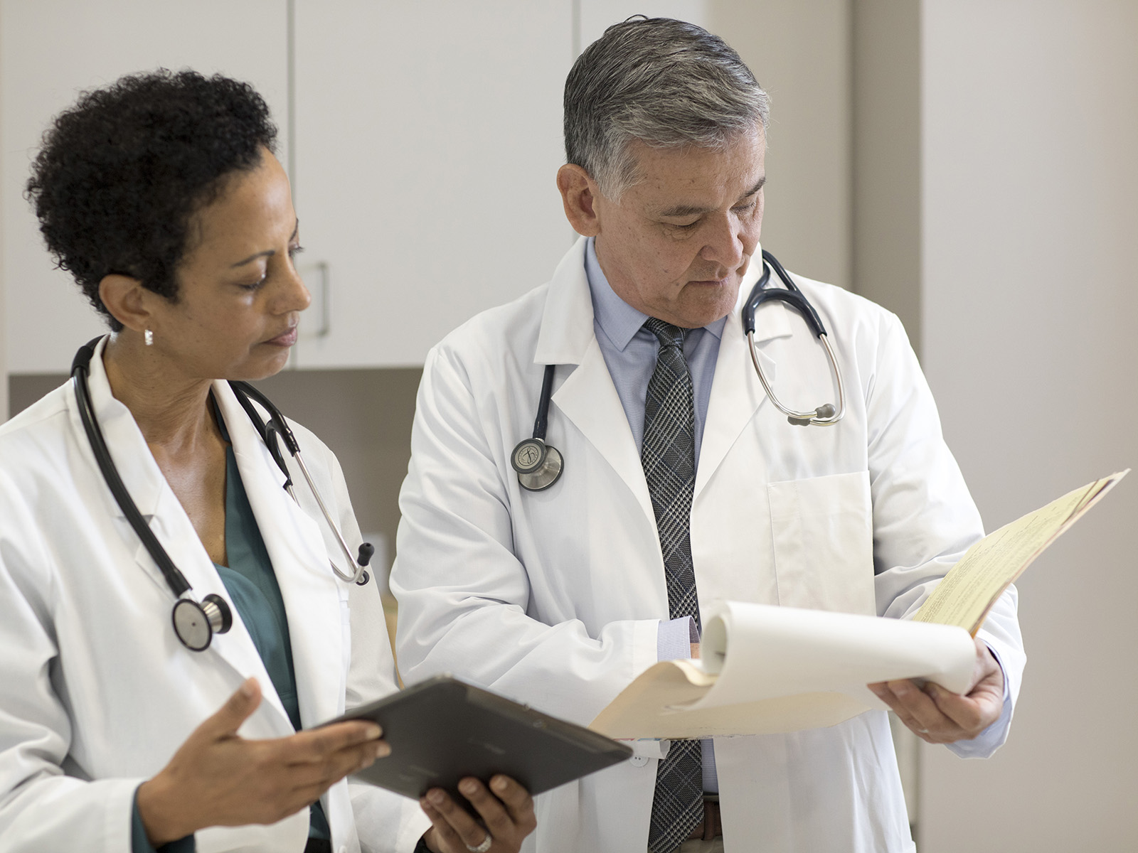 2 médicos con guardapolvos blancos conversan sobre la información en un expediente clínico.