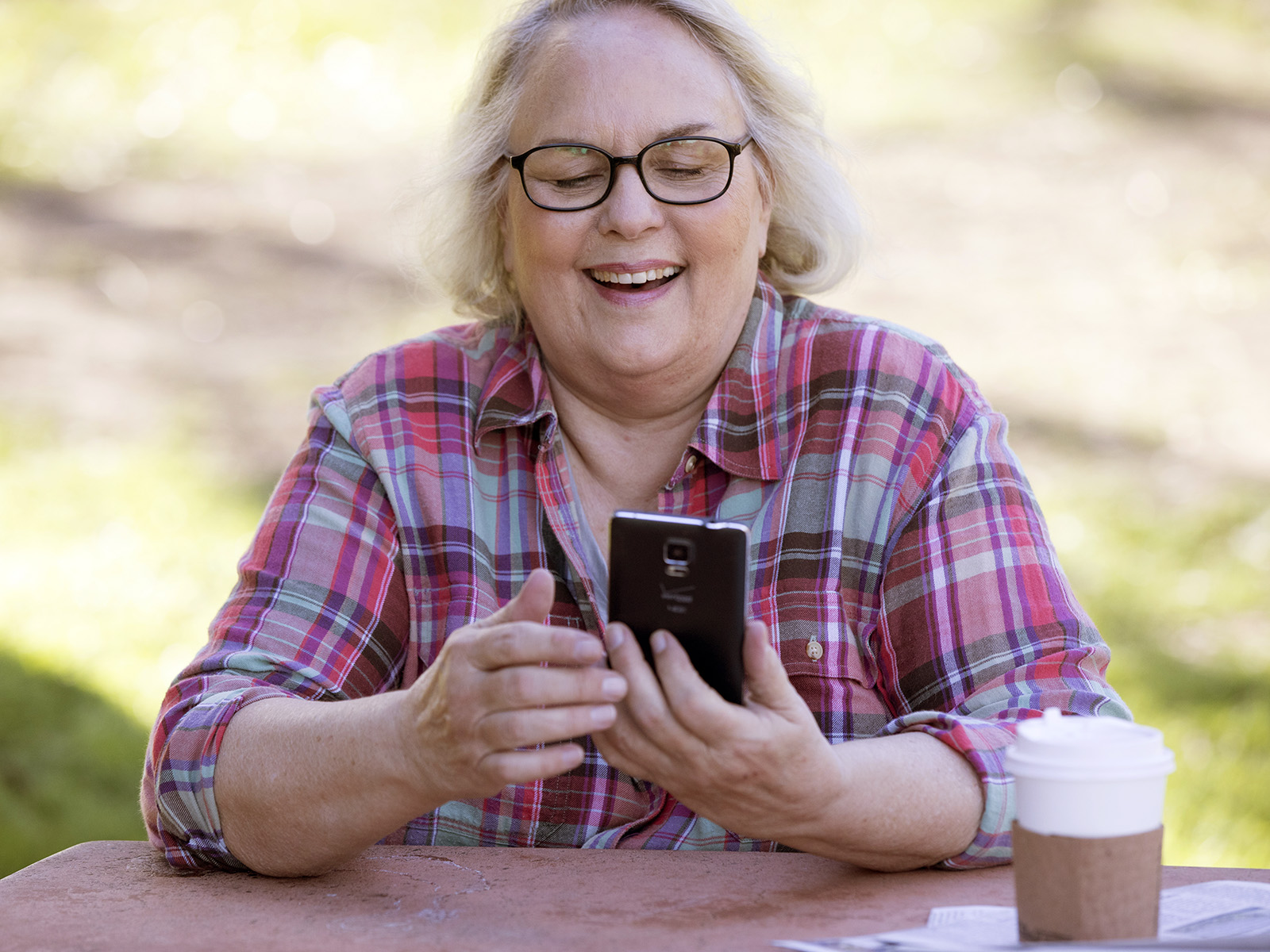 Una mujer se ríe de algo que está viendo en su teléfono, mientras está sentada en el parque.