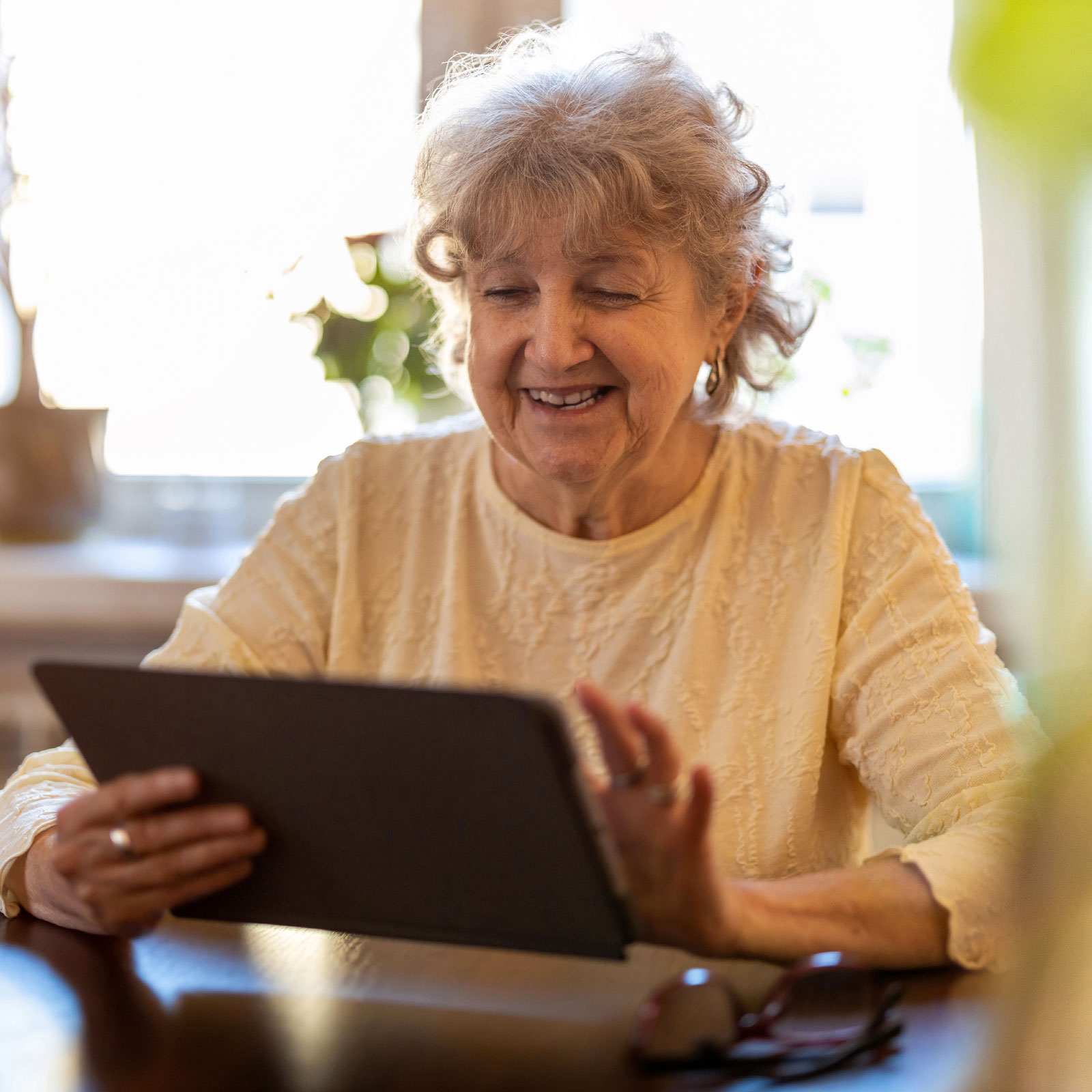 Older woman smiling using a tablet at a table.