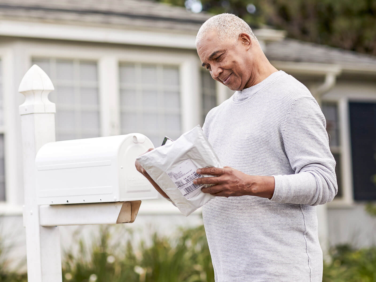 A man stands infront of his mailbox holding a package of a prescription.