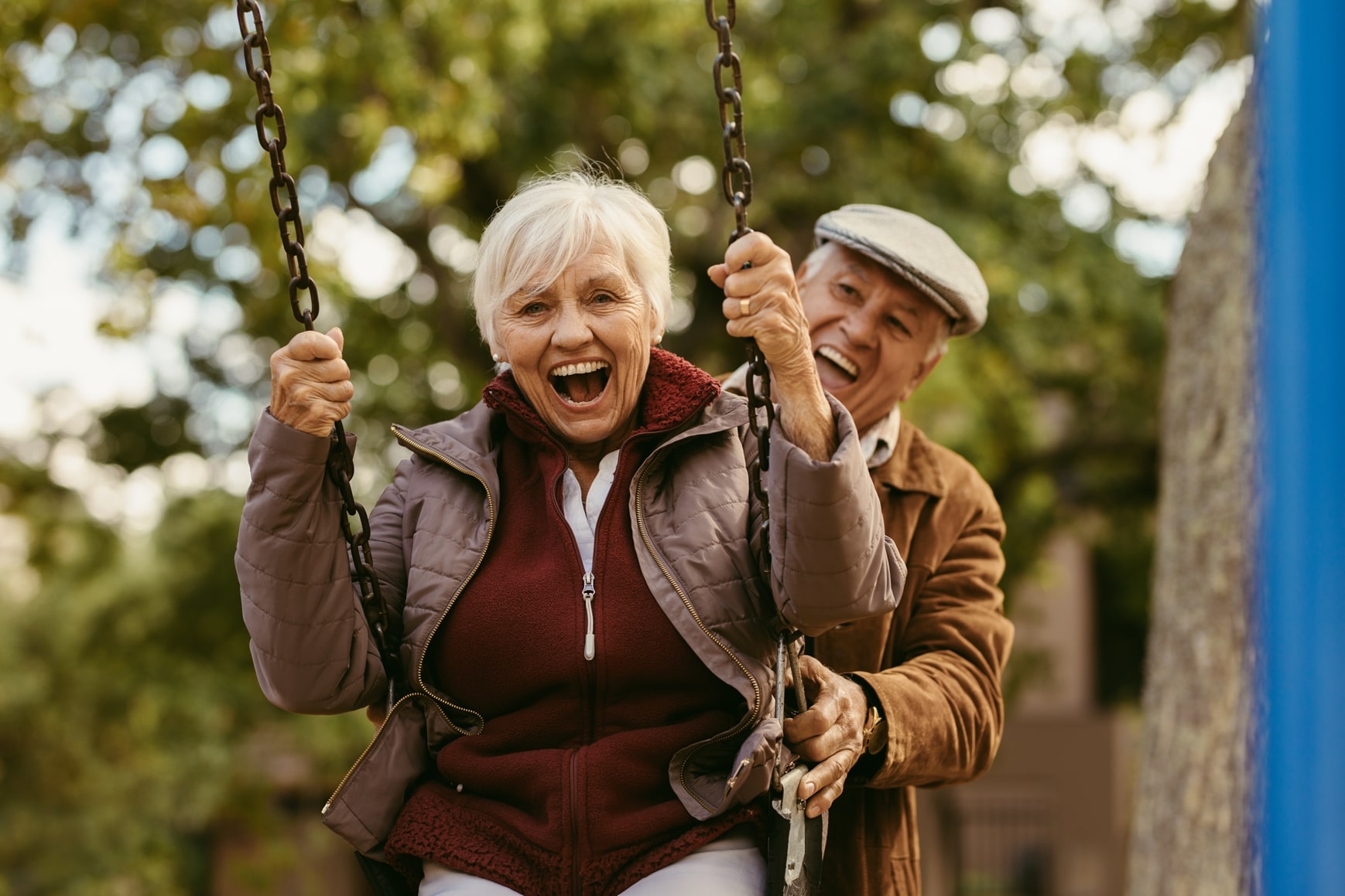 An elderly couple enjoy a swingset together.