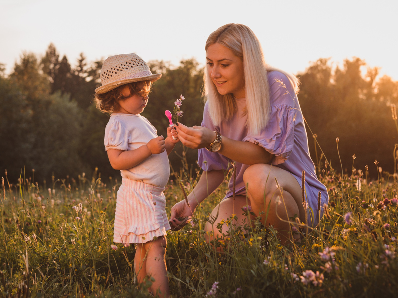 Mom picks wild flowers with young child in a field