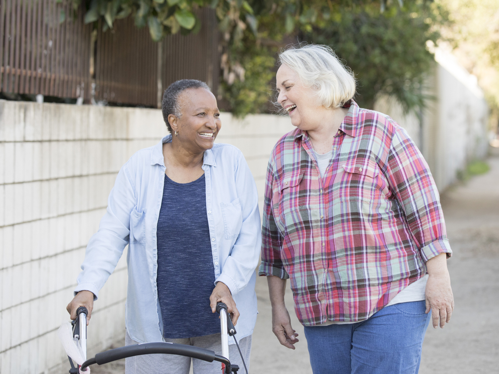 An older woman assisted by a walker enjoys a stroll outside with her caregiver.
