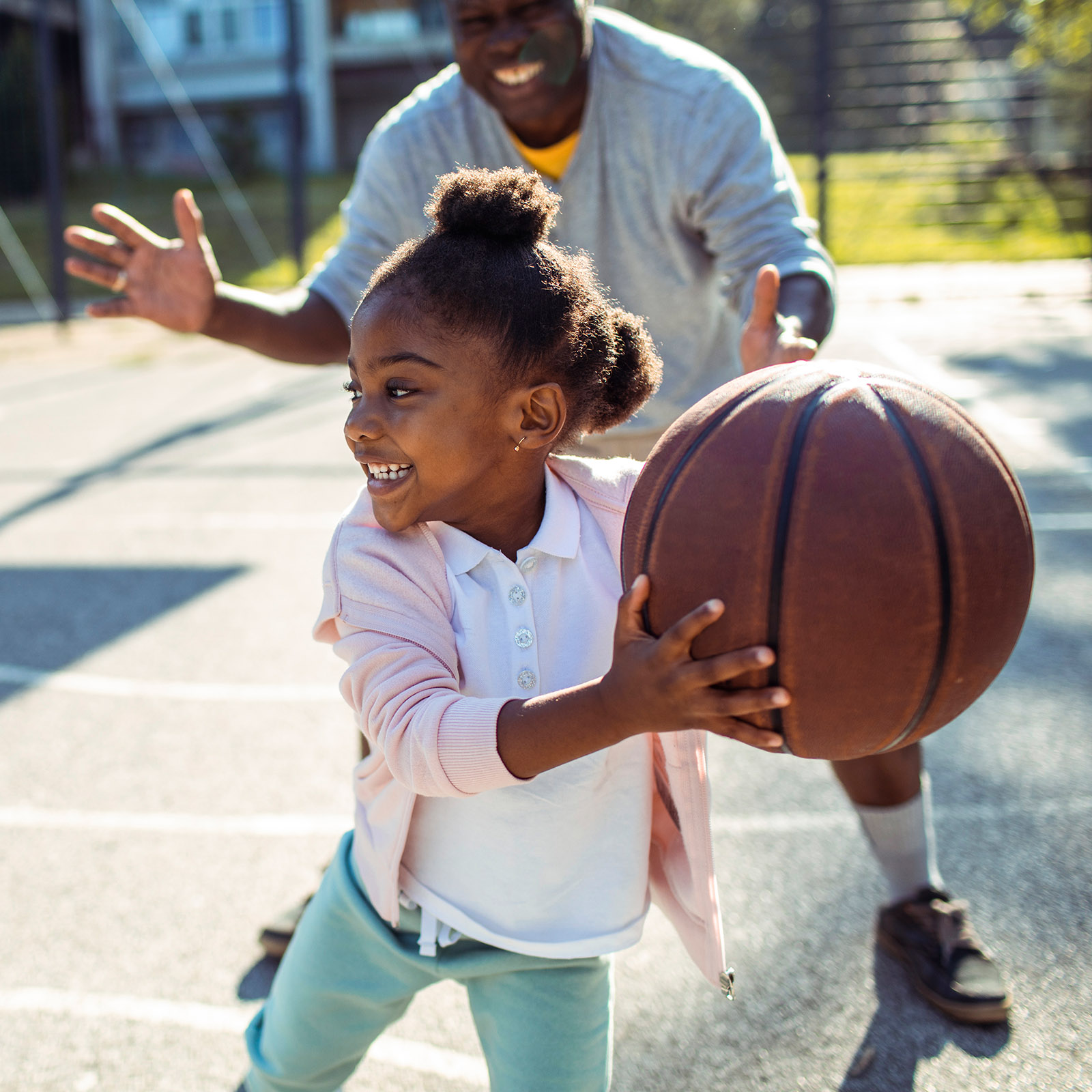 Dad plays basketball outside with daughter