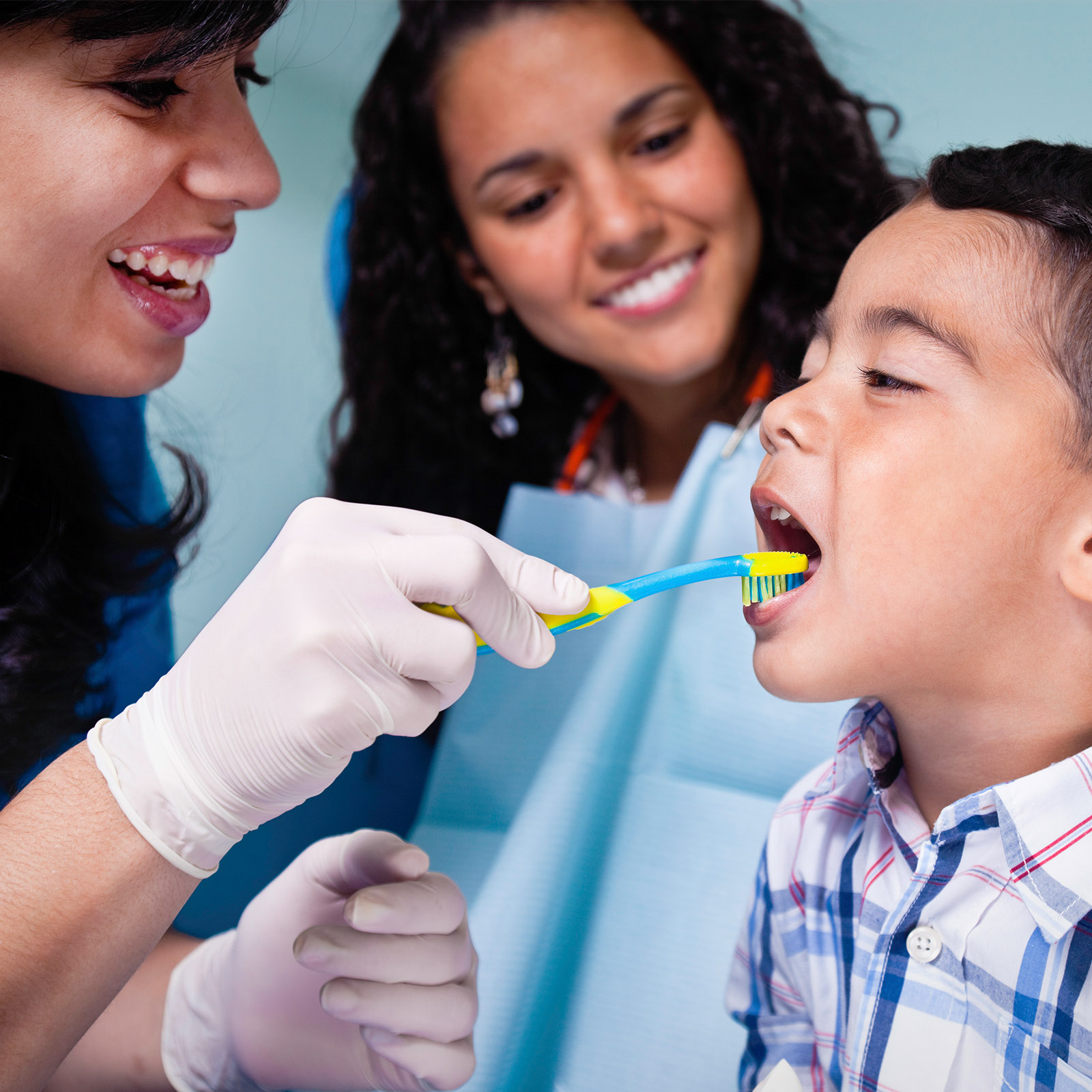 Dentista cepillándole los dientes a un niño mientras su mamá mira