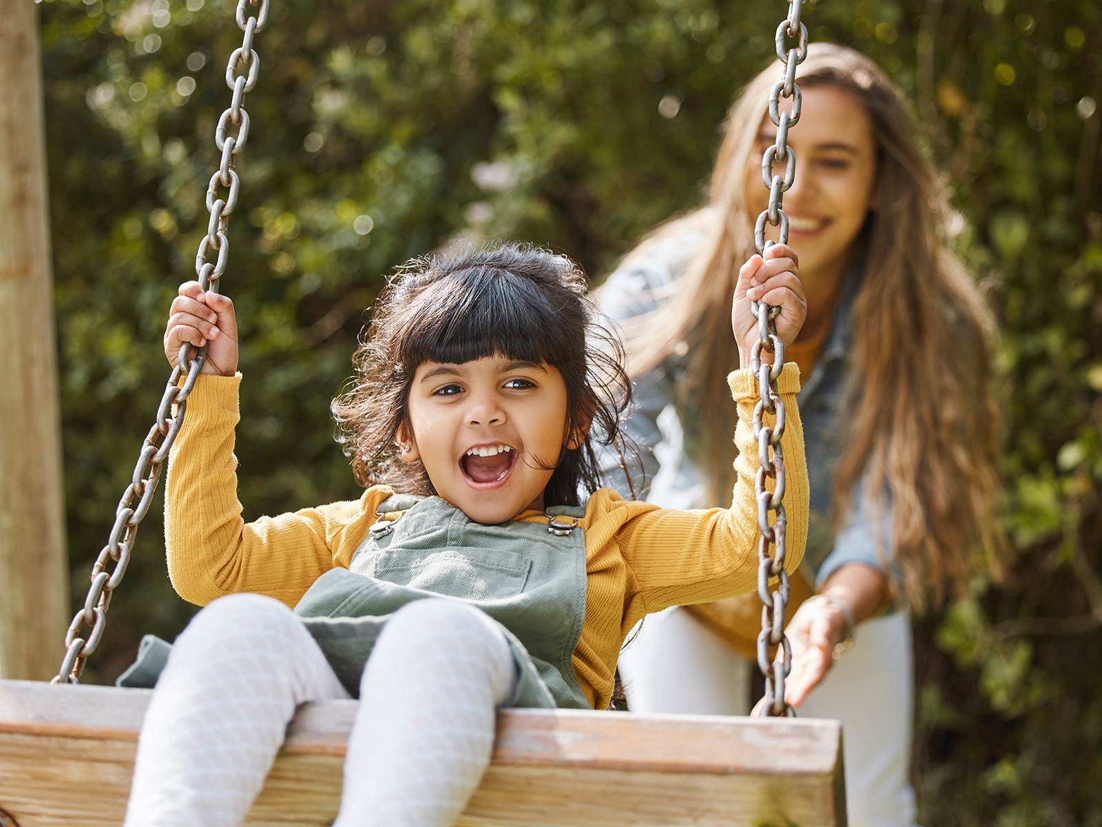 Child being pushed on a swing by an adult.