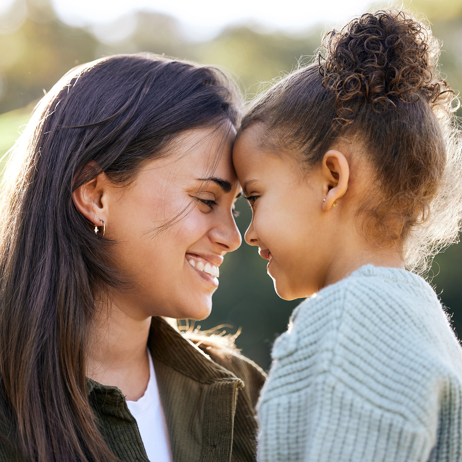 Mom holding daughter touching foreheads smiling while outside