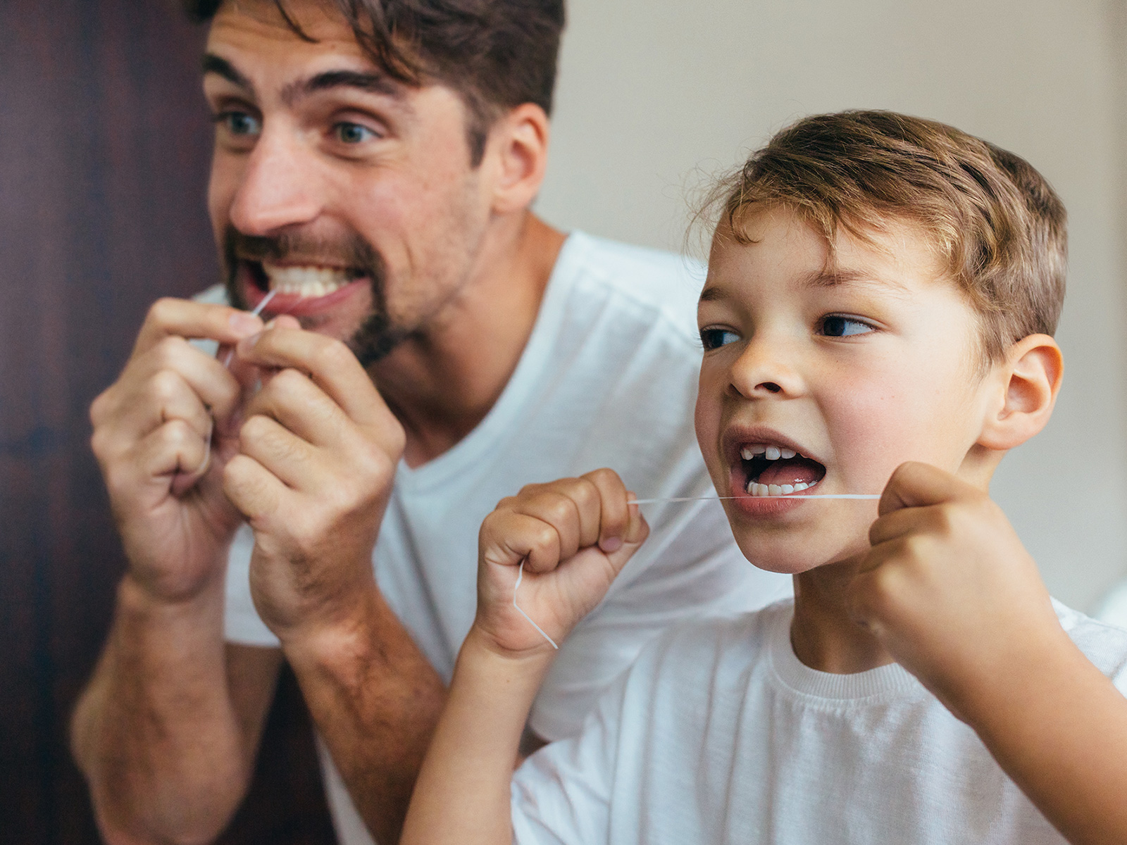 Padre e hijo limpiándose los dientes juntos con hilo dental.