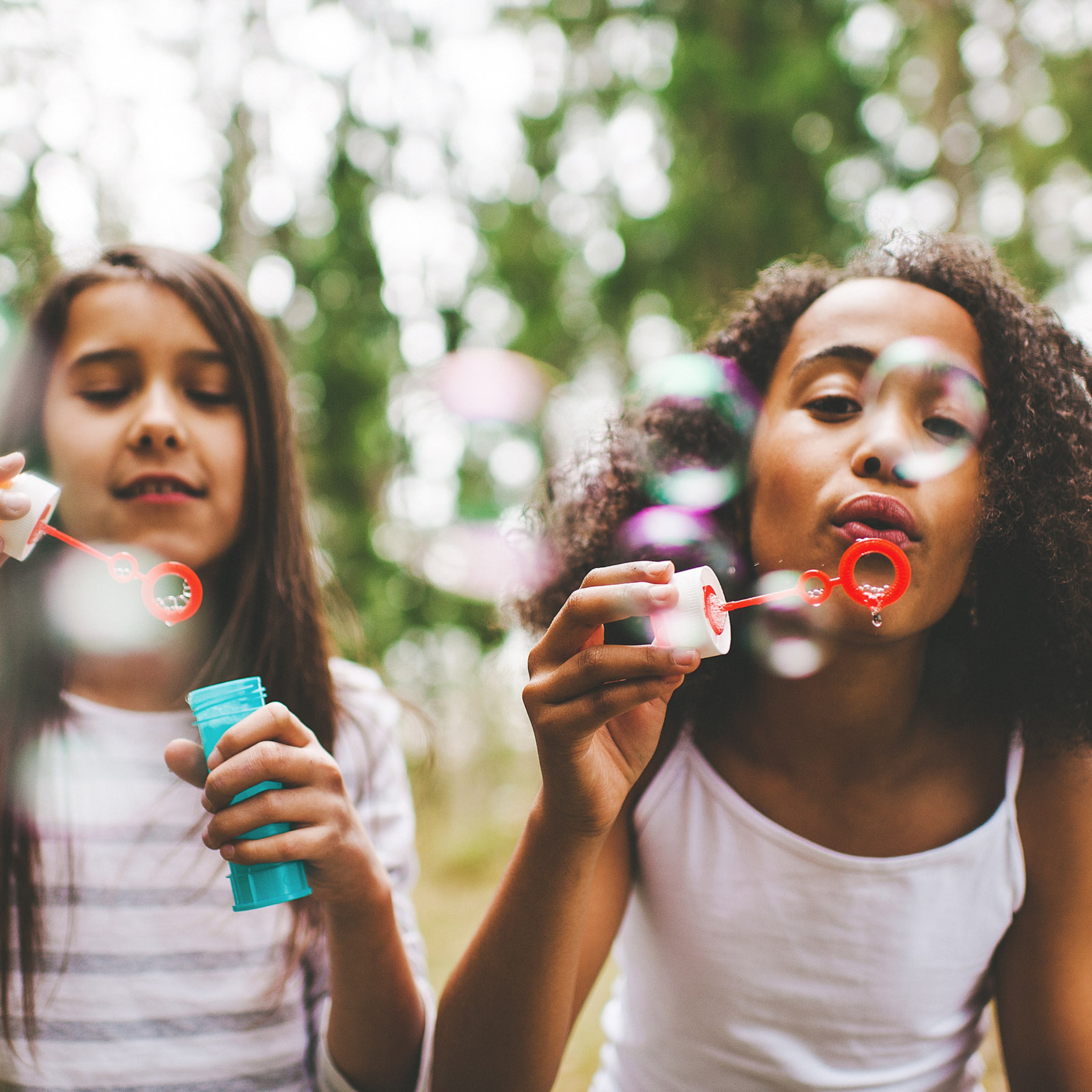 Two young girls blow bubbles outside