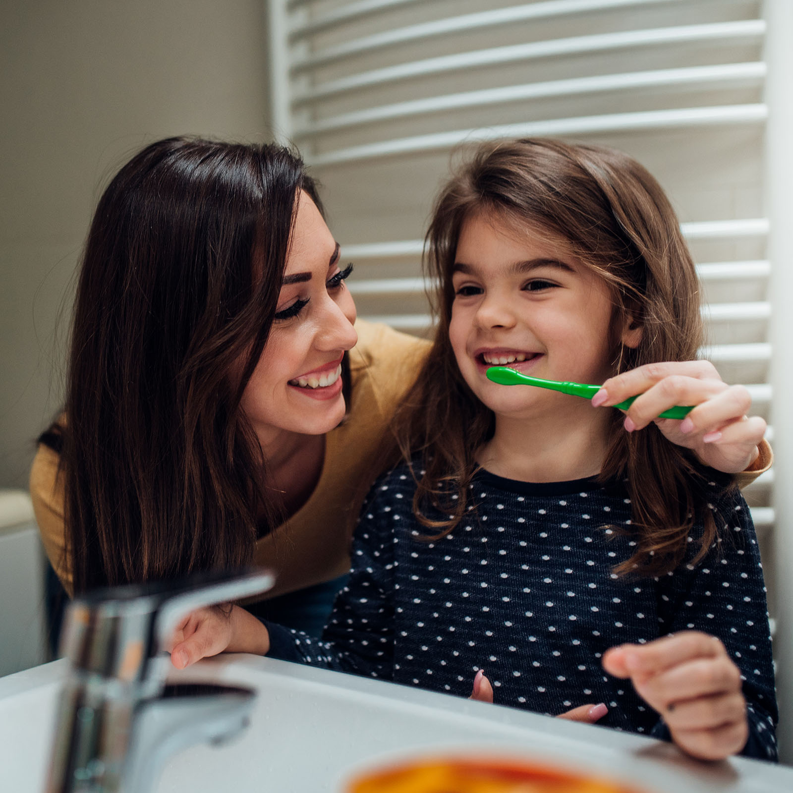 Mom helps her daughter brush her teeth