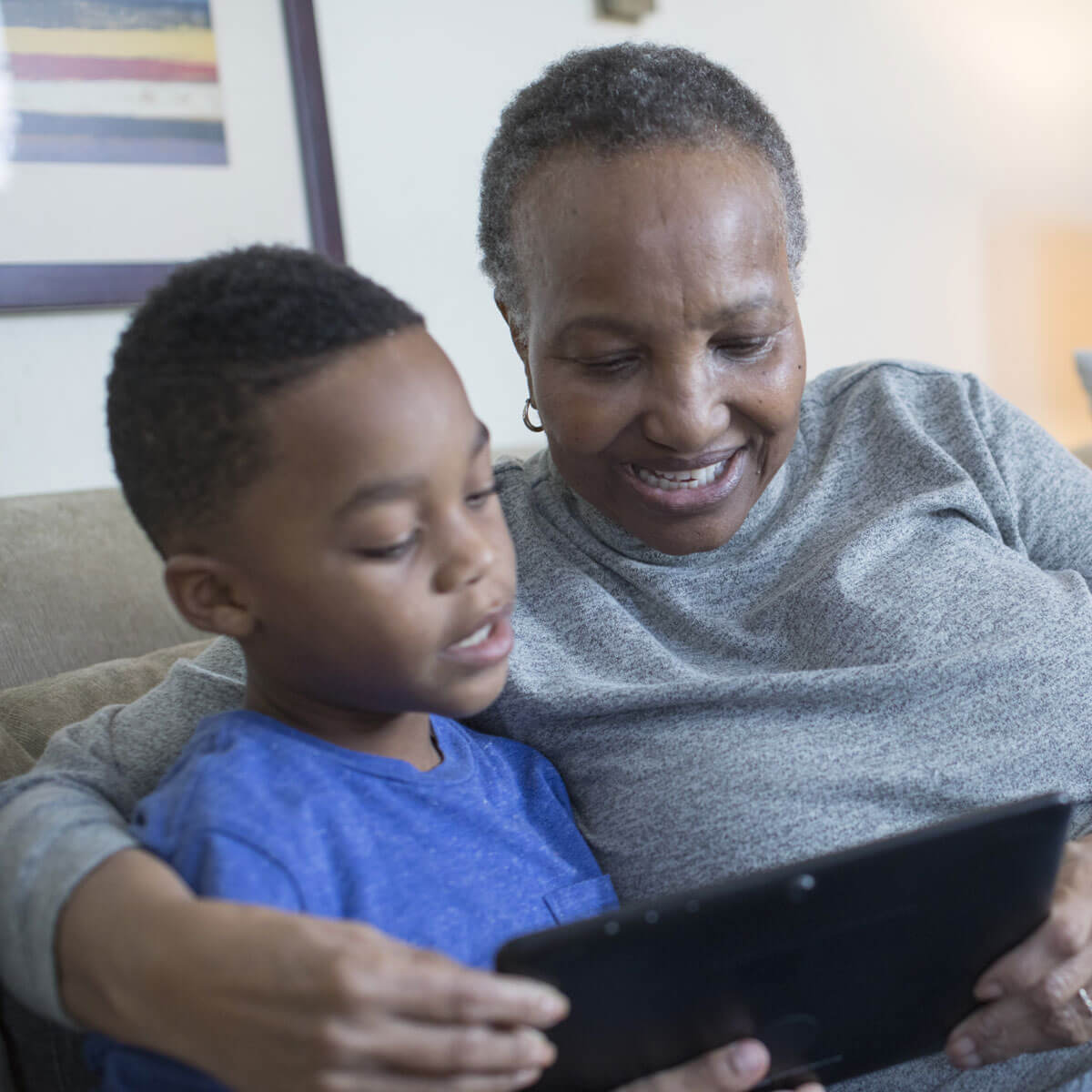 A grandmother and her grandson enjoy reading a book together on a couch.