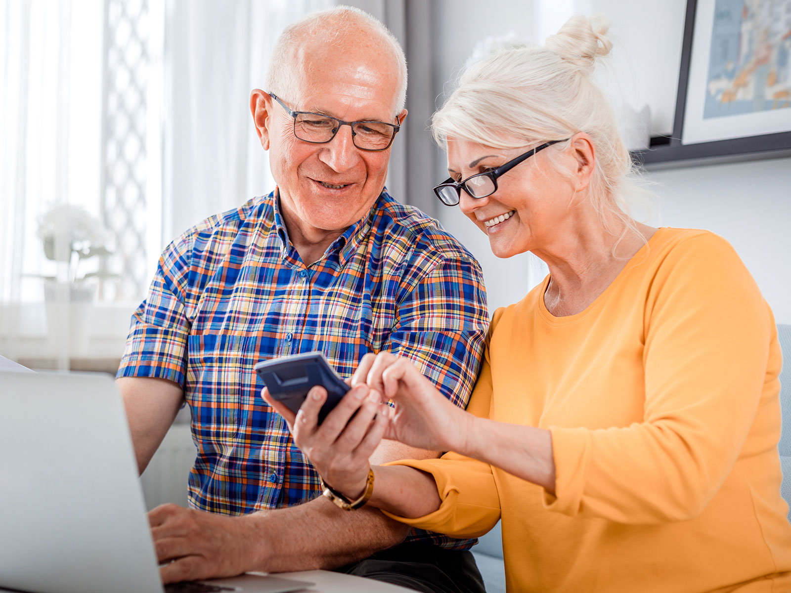 Older man and woman use phone and laptop.