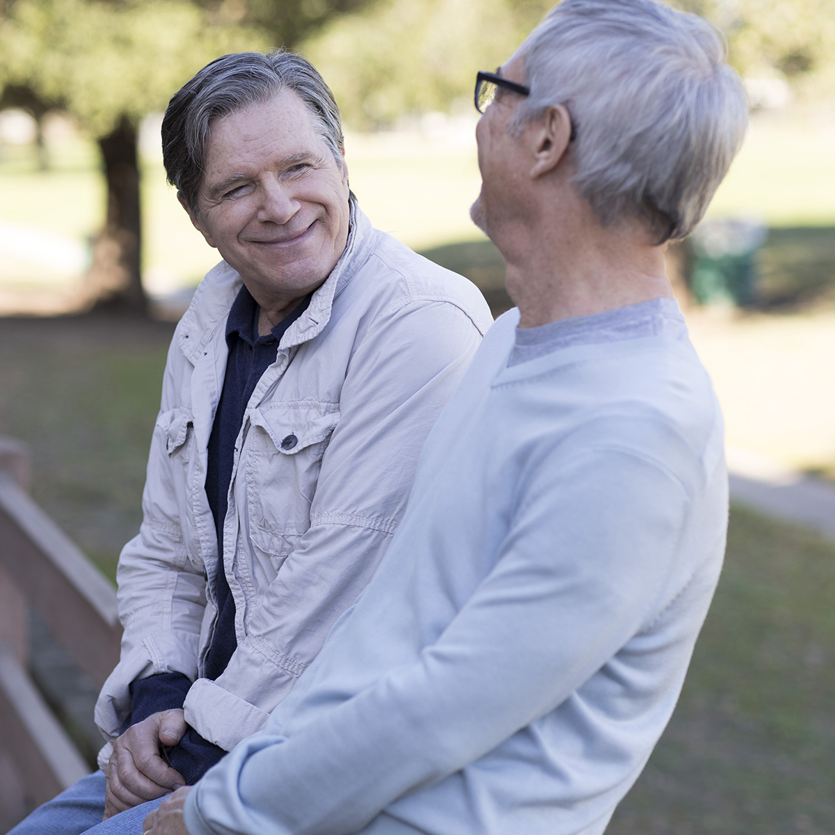 Two gentleman sitting on a park bench enjoying conversation and each other’s company.