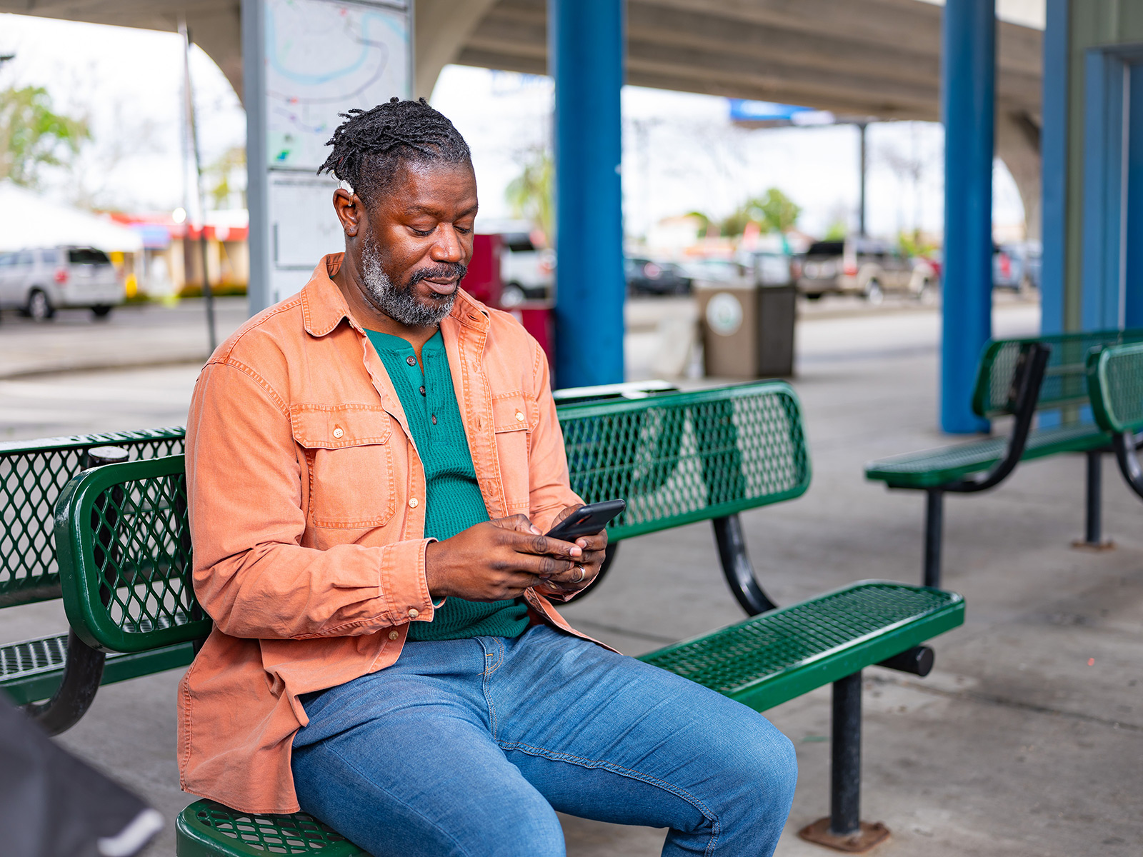 Afiliado de Medicaid usa el teléfono sentado en un banco de la ciudad
