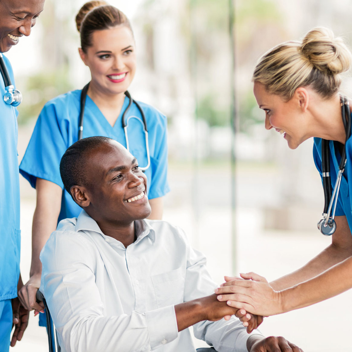 Hombre sonriente en una silla de ruedas, tomando la mano de una trabajadora de atención médica frente a él y otros dos profesionales sonrientes detrás.