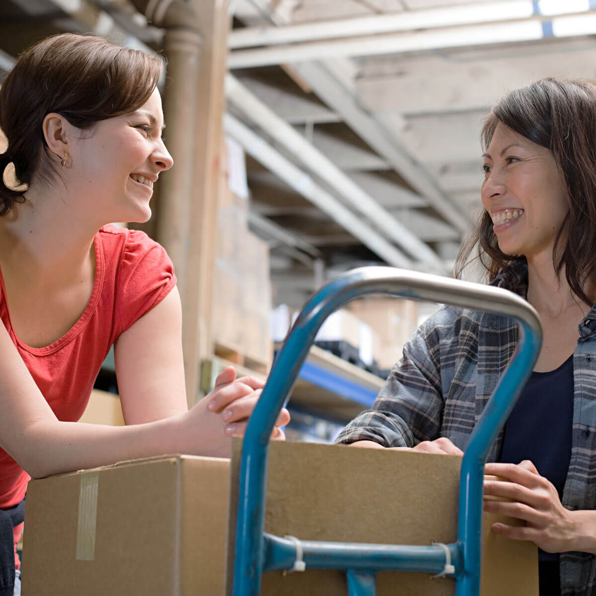 Two Humana suppliers in a warehouse smile as they talk and collect packages for an order.