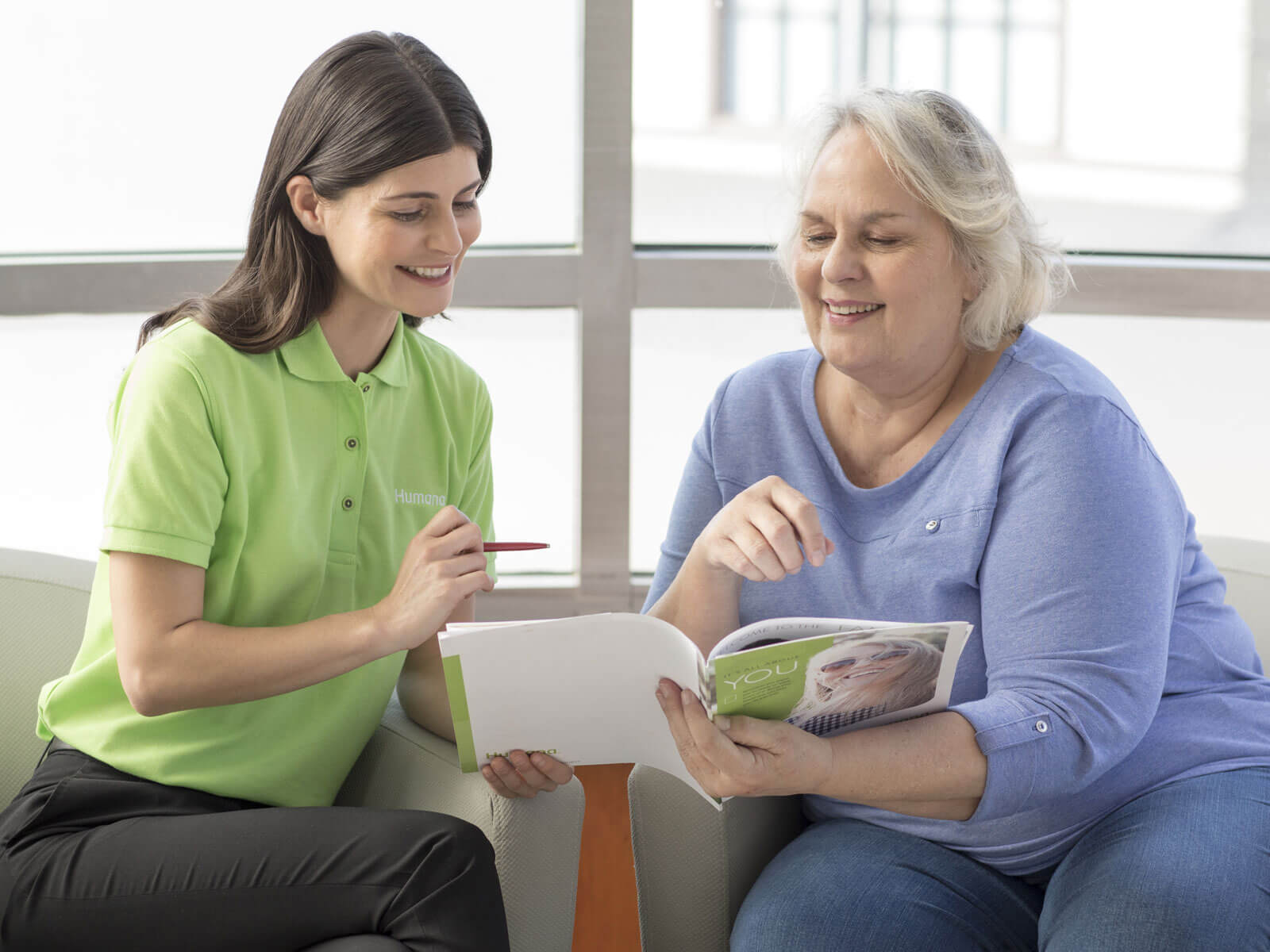 Un empleado de Humana ayuda a una mujer a entender los planes de seguro médico detallados en un folleto.