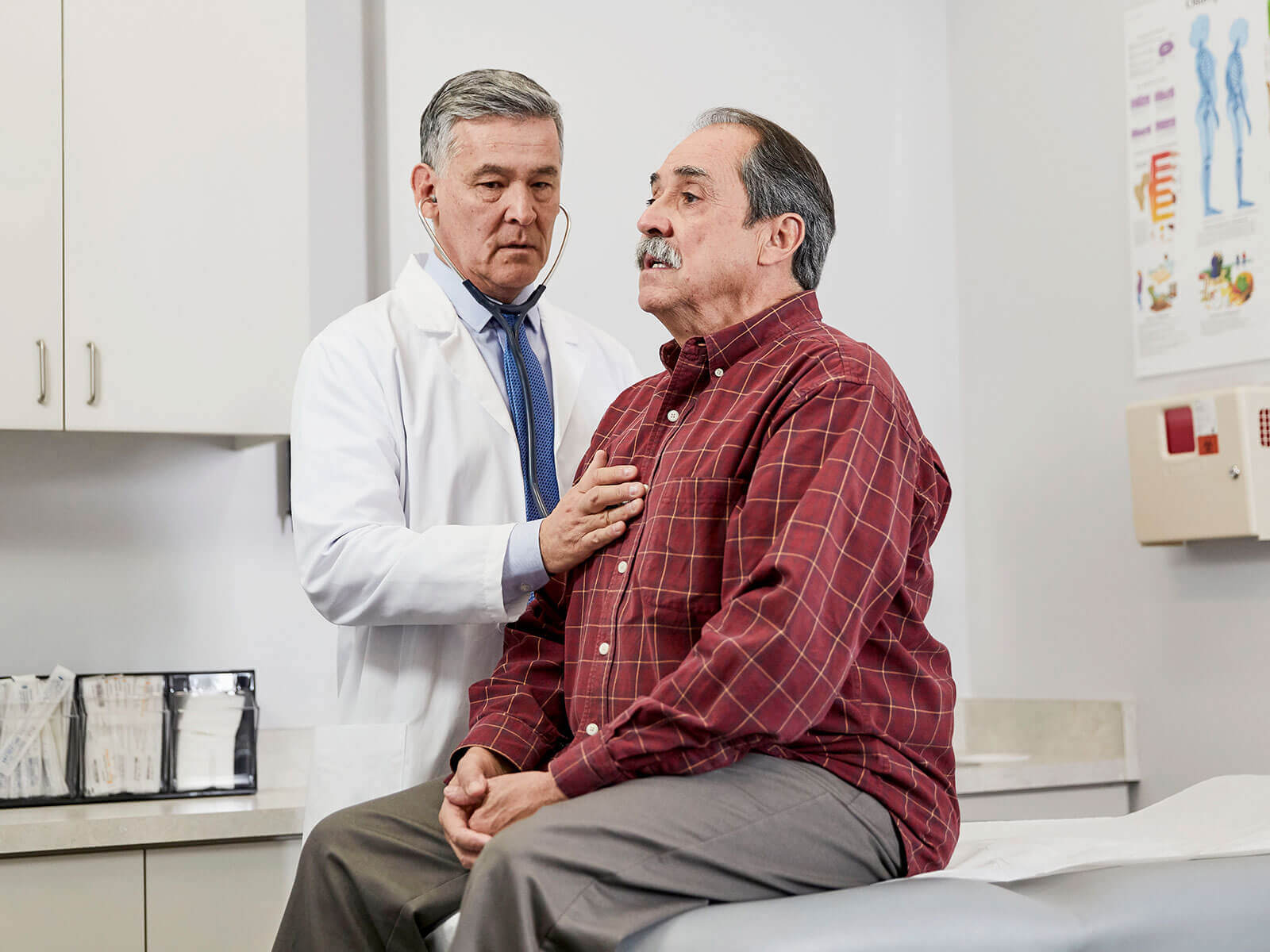 A doctor checks a man’s heartbeat with a stethoscope in an examination room.